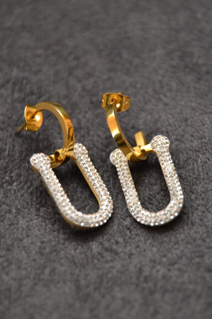 Close-up of sparkling gold and diamond hoop earrings on a textured surface.